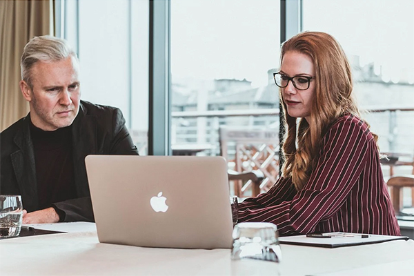 image of two people working together on a laptop, pens and paper